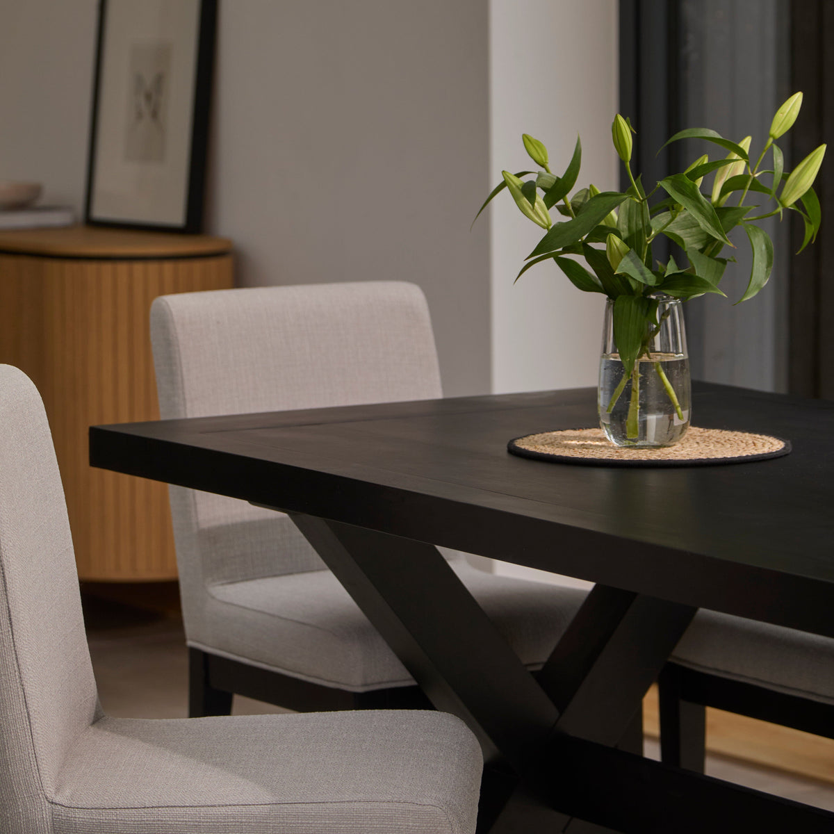 Dining room with a dark wooden table, boucle chairs, and a vase with green leaves.